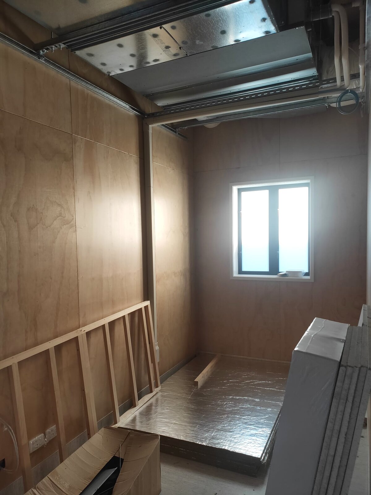 A module interior at lining stage, with plywood walls, exposed framing and ceiling services