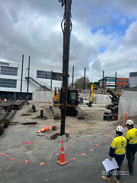 A piling rig at work on the Pacific Rise site, with two workers in hi-vis looking on