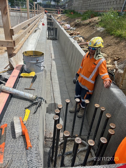 A worker beside the retaining wall trench, with drainage matting and starter bars in place